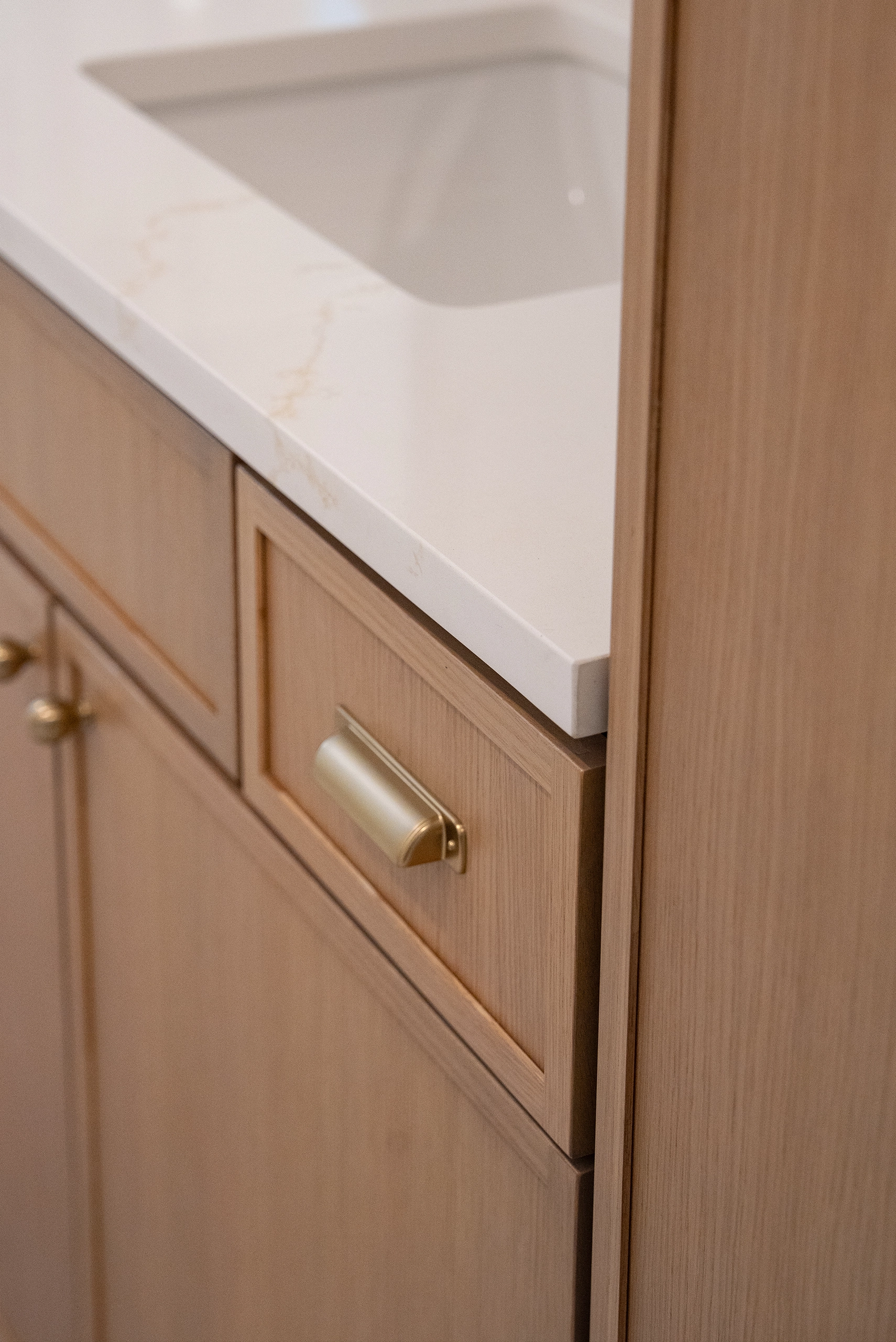 Modern bathroom design detail showing a white quartz countertop edge sitting on a natural wood vanity cabinet.