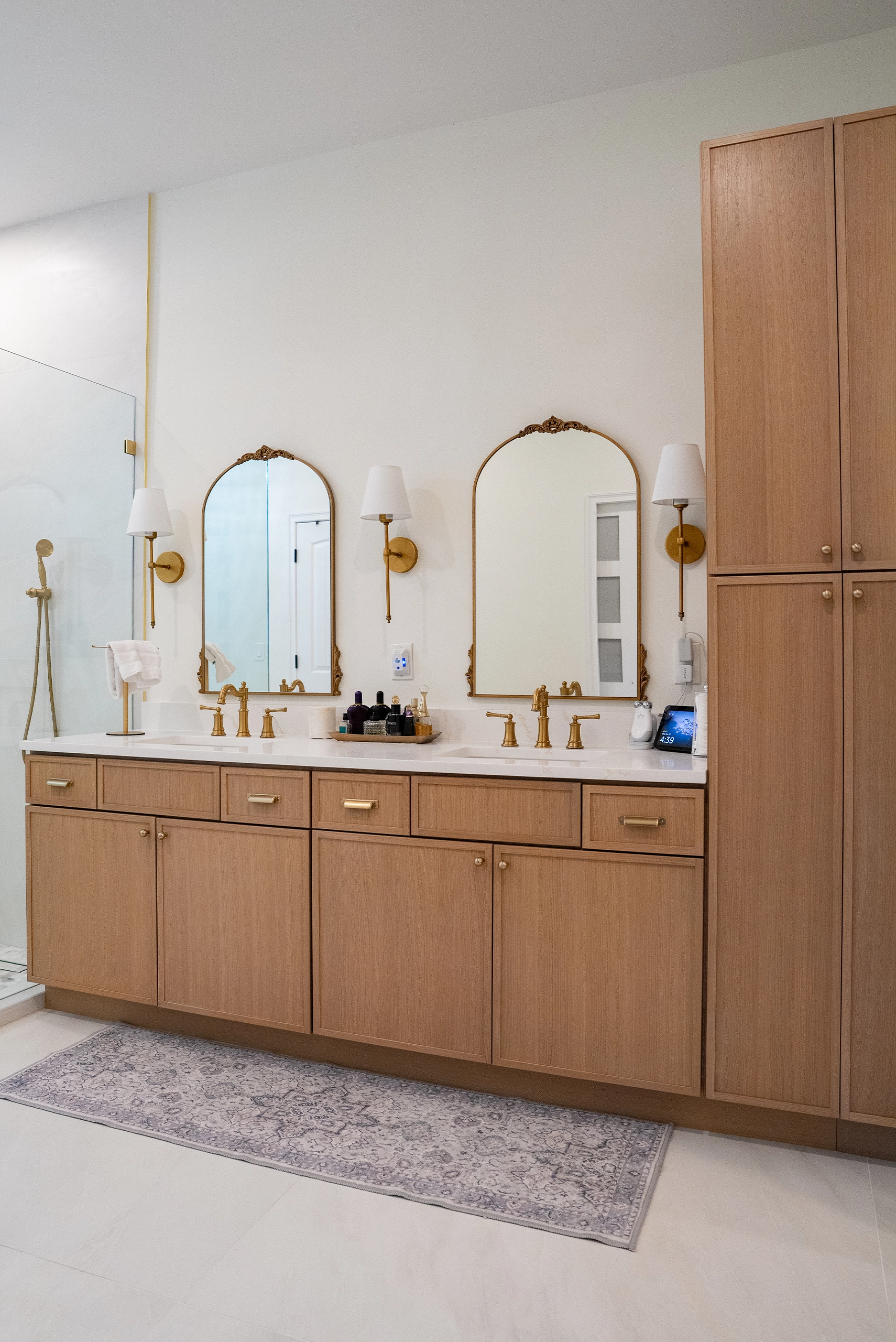 Warm transitional bathroom interior showcasing natural wood cabinetry, gold faucets, and a patterned runner rug.
