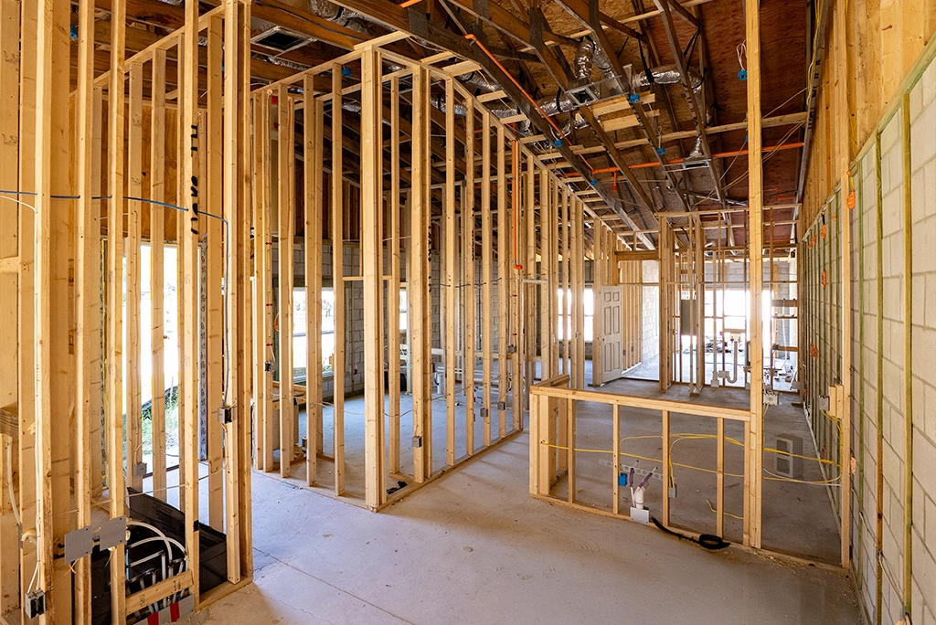 Interior view of a residential construction site during the framing stage, featuring wooden wall studs and ceiling joists.