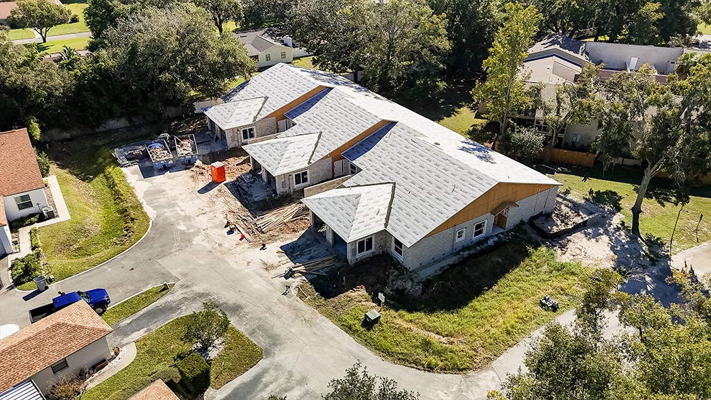 Aerial view of a new residential construction site with concrete block walls and roofing underlayment installation in progress.
